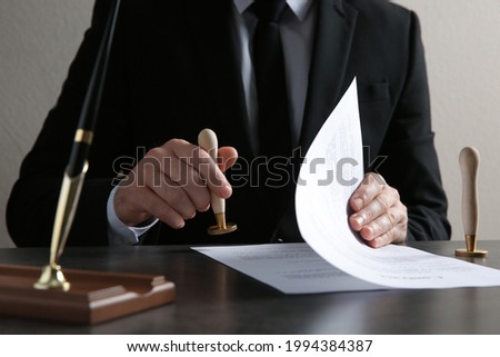 Male notary stamping document at table, closeup