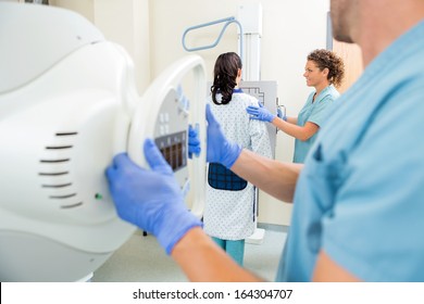 Male nurse adjusting xray machine with colleague and patient in examination room