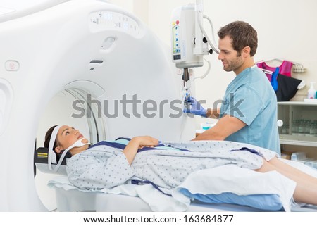 Male nurse looking at patient undergoing CT scan test in examination room