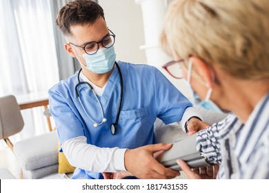 Die männliche Krankenschwester misst den Blutdruck einer älteren Frau mit Maske während ihres Besuchs zu Hause.