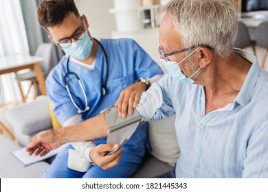Die männliche Krankenschwester misst den Blutdruck auf den hohen Mann mit Maske während des Besuchs zu Hause.