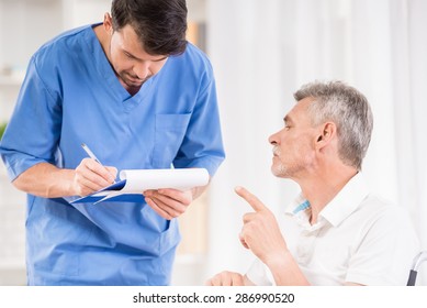 Male Nurse Taking Care About Senior Patient In Wheelchair.
