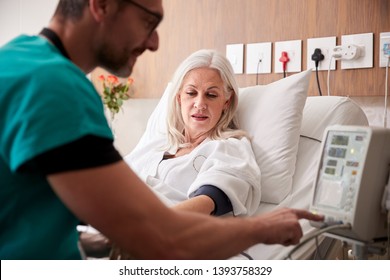 Male Nurse Taking Mature Female Patients Blood Pressure In Hospital Bed With Automated Machine