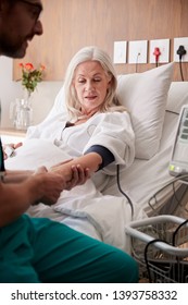 Male Nurse Taking Mature Female Patients Blood Pressure In Hospital Bed With Automated Machine