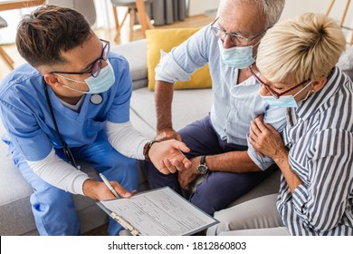 Male Nurse Talking To Seniors Patients With Mask While Being In A Home Visit.