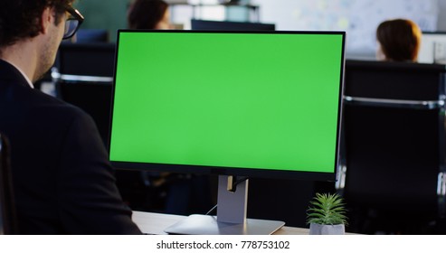 Male Office Employee Working On The PC Computer With Green Screen In The Office Room. View From Behind. Chroma Key. Indoors