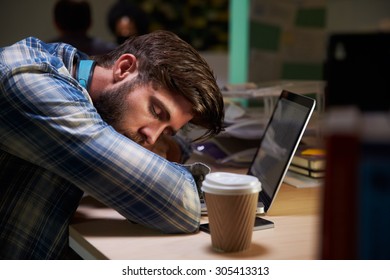 Male Office Worker Asleep At Desk Working Late On Laptop