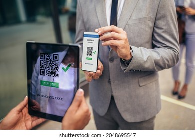 Male Office Worker In Safety Mask Showing Electronic Vaccination Certificate To Employer