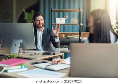 Male Office Worker Waving Hi To Colleague Sitting At Neighboring Table