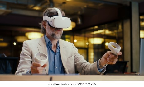 Male office worker wearing VR headset and using wireless controllers and laptop, gesturing, watching data in virtual reality. Work in modern office of hi-tech company. Cyberspace digital technology - Powered by Shutterstock