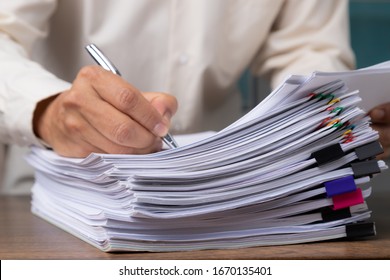 Male office workers with yellow shirt holding and writing documents on office desk, Stack of business overload paper. - Shutterstock ID 1670135401