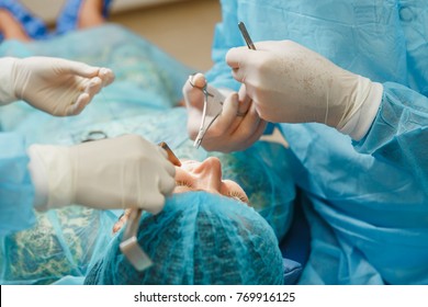 Male Old Professional Dentist Surgeon In Uniform And Female Assistant Helps To Performing Operation Install Dental Implant Teeth Of Woman Patient In Clinic Light Office With Modern Tools Equipment