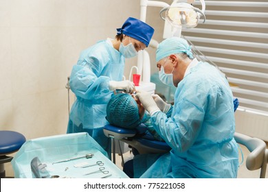 Male Old Professional Dentist Surgeon In Uniform And Female Assistant Helps To Performing Operation Install Dental Implant Teeth Of Woman Patient In Clinic Light Office With Modern Tools Equipment