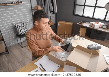 Male online store seller packing bag at table in warehouse
