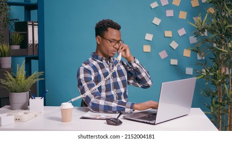 Male operator answering landline phone call in office, talking to people at customer support service. Man using vintage retro telephone to dial contact number and chat with client.