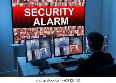 Male Operator Monitoring Multiple CCTV Footage With Security Alarm Text On Screen