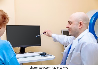 A Male Ophthalmologist Explains The Results Of An Eye Examination To An Adult Woman, Showing A Drawing On A Computer.