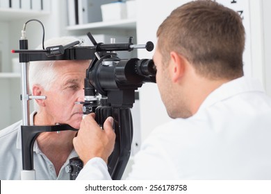Male optician examining senior patients eyes through slit lamp in clinic