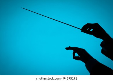 Male Orchestra Conductor Hands, One With Baton. Silhouette Against Blue Background.