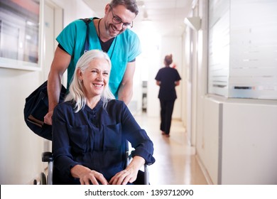 Male Orderly Pushing Senior Female Patient Being Discharged From Hospital In Wheelchair