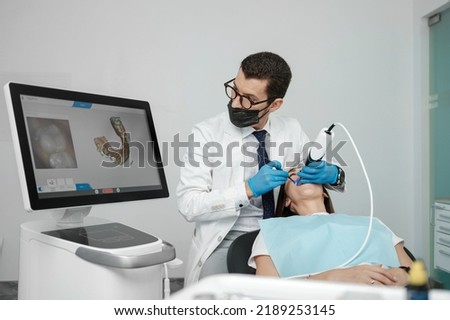 Male orthodontist scaning patient with dental intraoral scanner and controls process on screen. Prosthodontics and stomatology concept.