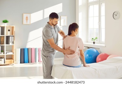 Male osteopath examining young woman in modern office. Young physiotherapist doing healing treatment on woman back in rehabilitation clinic. Chiropractor helping patient with scoliosis and back pain. - Powered by Shutterstock