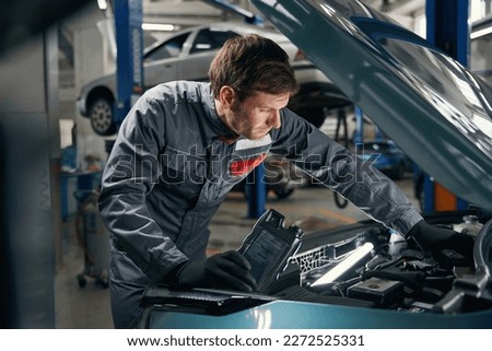 Male in overalls working near the automobile