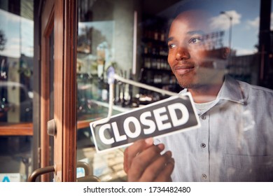 Male Owner Of Coffee Shop Or Restaurant Turning Round Closed Sign On Door Of Failed Business