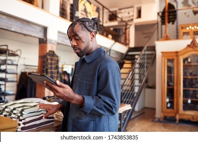 Male Owner Of Fashion Store Using Digital Tablet To Check Stock In Clothing Store