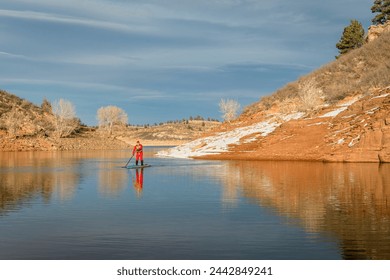 male paddler in red drysuit is paddling a stand up paddleboard on mountain lake in Colorado, winter scenery - Powered by Shutterstock