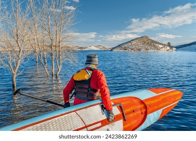 male paddler wearing a drysuit, life jacket and safety leash  is starting workout on a long racing stand up paddleboard on a mountain lake in Colorado - Horsetooth Reservoir in winter conditions - Powered by Shutterstock
