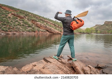 male paddler with a wooden canoe paddle and waterproof duffel on a rocky lake shore - Horsetooth Reservoir in northern Colorado