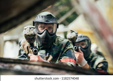 male paintballer and his team in uniform and protective masks aiming by paintball guns outdoors