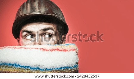 Male painter in hard hat with paint roller. Closeup portrait of painter, contractor or decorator in protective helmet with paintroller. Room painting job. To make repairs. Copy space for advertising.