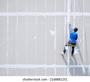 Male painter is using rappelling rope to paint tall buildings, specialized work where danger and accident prone, safety protection is not up to standard.