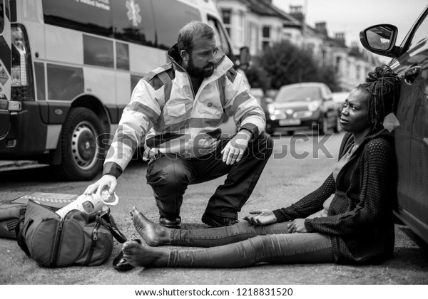 Male\
paramedic checking on an injured woman on a\
road