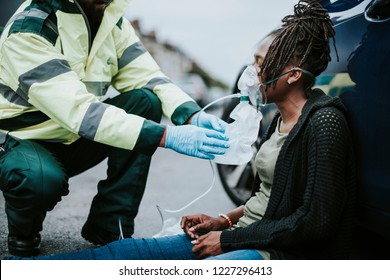 Male Paramedic Putting On An Oxygen Mask To An Injured Woman On A Road