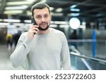 Male passenger in casual clothing talking on his mobile phone next to the subway escalator in subway