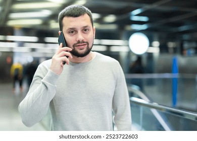 Male passenger in casual clothing talking on his mobile phone next to the subway escalator in subway - Powered by Shutterstock