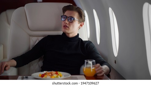 Male Passenger Having Meal In First Class. Young Handsome Businessman Relaxing In Leather Chair Having Lunch Flying Business Class