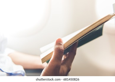Male passenger killing time by reading book while traveling on the plane