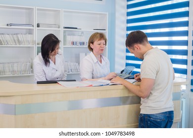 Male Patient With Doctor And Nurse At Reception Desk In Hospital