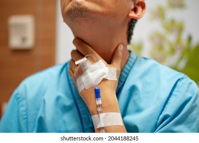 A male patient a hand with iv line holds on his neck. laryngitis, goiter, hypothyreosis or toxic thyroid treatment at the hospital.