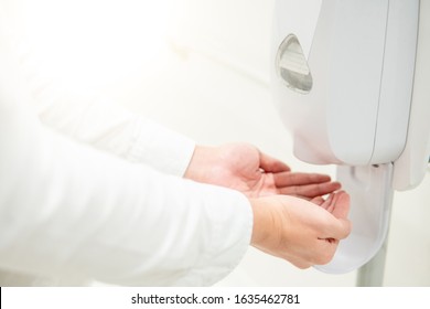 Male patient hands using automatic alcohol dispenser for cleaning hand in the hospital. Infection prevention concept. Save and clean in public medical center area.