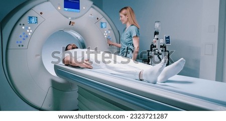 Male patient lies at TC scanner bed. Man goes out of MRI capsule. Female doctor dressed up in uniform have talk with patient. Medical worker smiling and pushes buttons of MRI capsule.