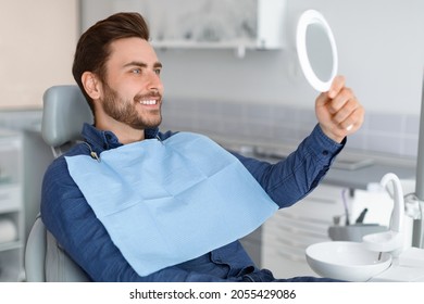 Male Patient Looking At His Beautiful Healthy White Smile, Holding Dental Hand Mirror, Happy Young Man Checking Results Of Treatment At Modern Dentistry, Using Hand Mirror, Side View