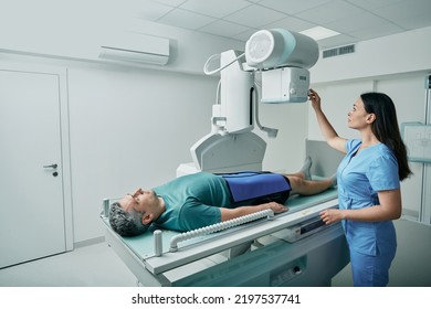 Paciente varón acostado en la cama mientras una enfermera ajustaba una máquina de rayos X moderna para escanear su pierna o rodilla en busca de lesiones y fracturas