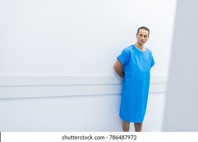 Male Patient In Medical Gown Standing At Wall In Hospital 