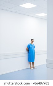 Male Patient In Medical Gown Standing At Wall In Hospital 