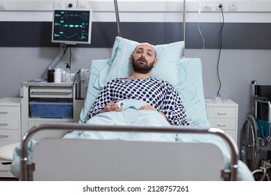 Male Patient Recovering Lying In Hospital Bed Recieving Medication Through Iv Drip Line After Surgical Intervention. Man With Respiratory Problems Connected To Vitals Monitor And Pulse Oximeter.